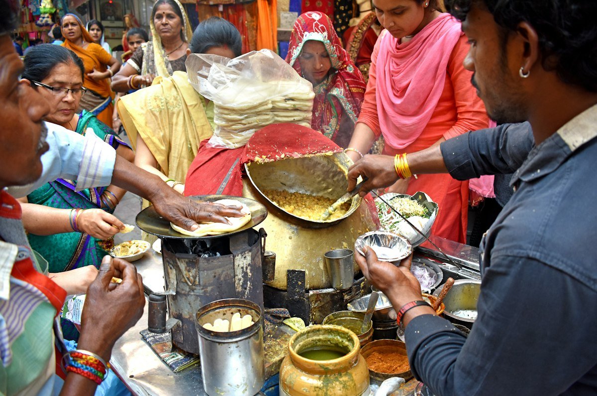 A crowd of people cooking and serving food together at a large outdoor kitchen