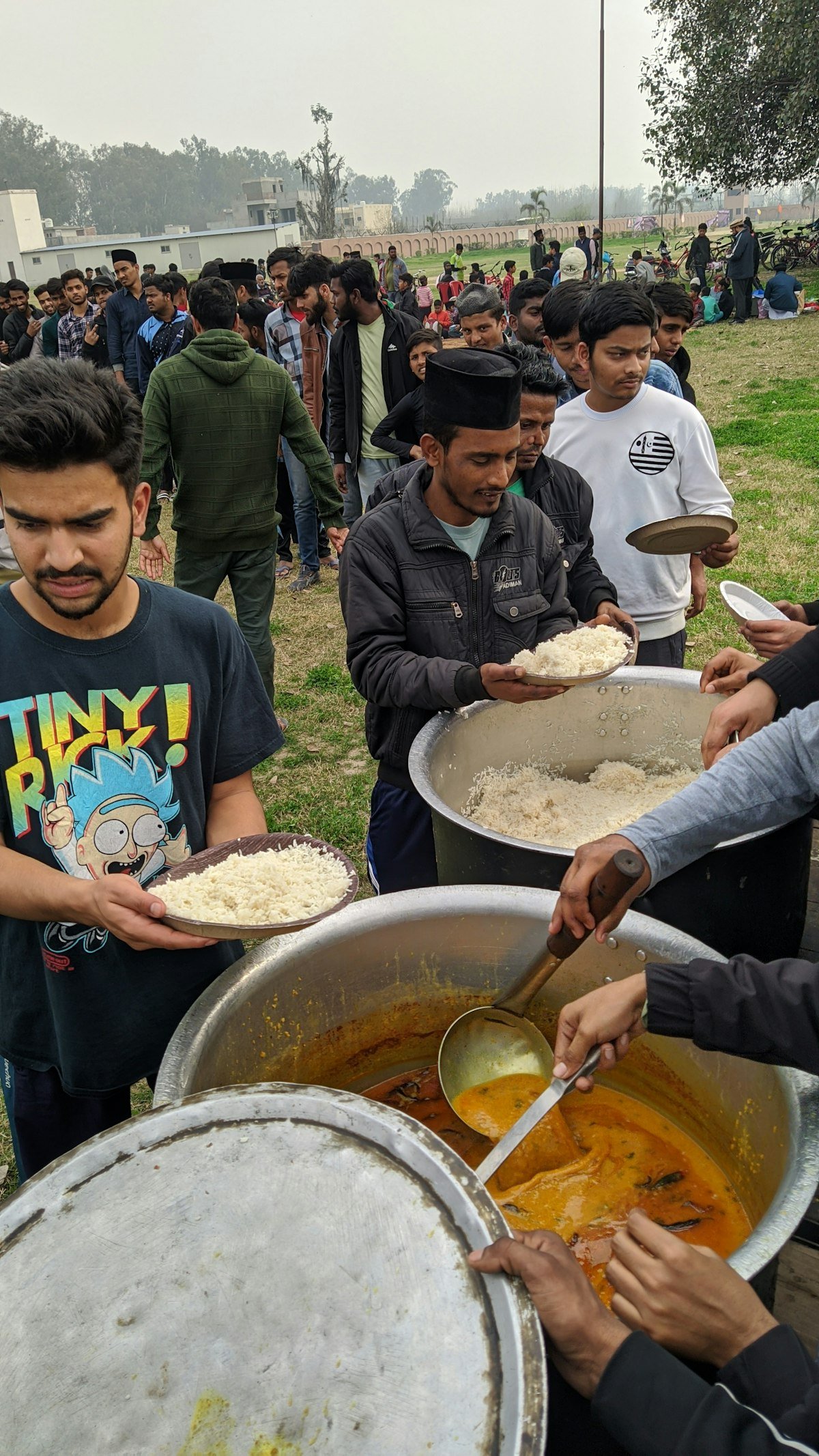 Volunteers serving rice from a large pot to people at a community meal