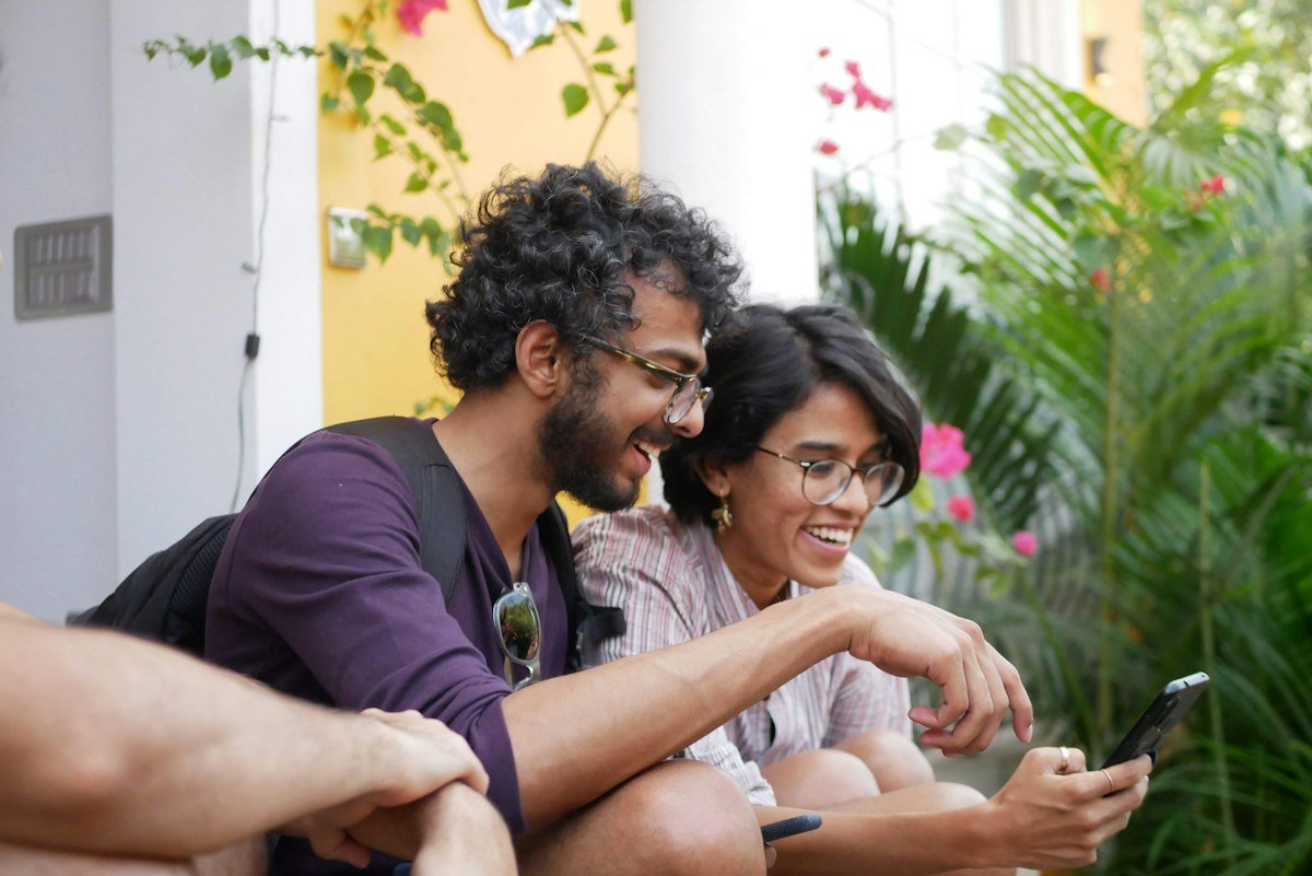 An Indian man and woman laughing while looking at a smartphone outdoors