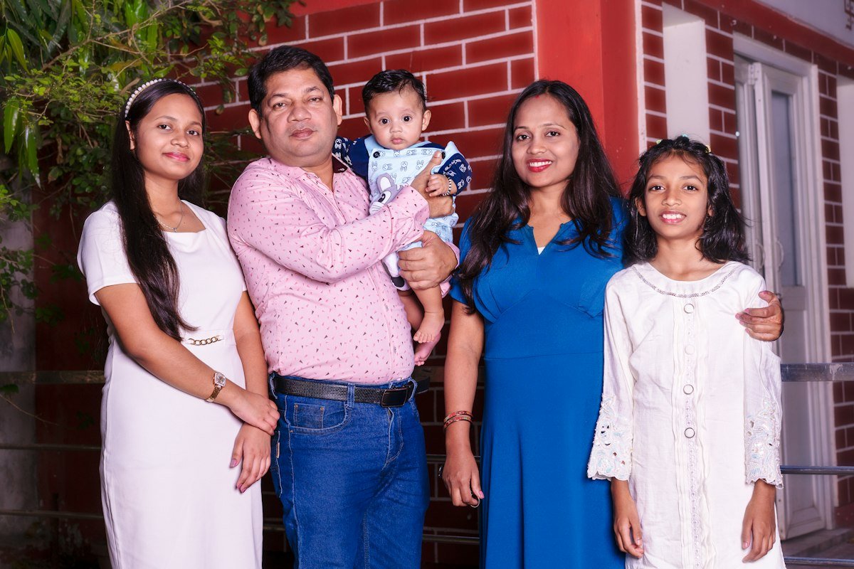 A family of five, parents with three children, standing together outside their home
