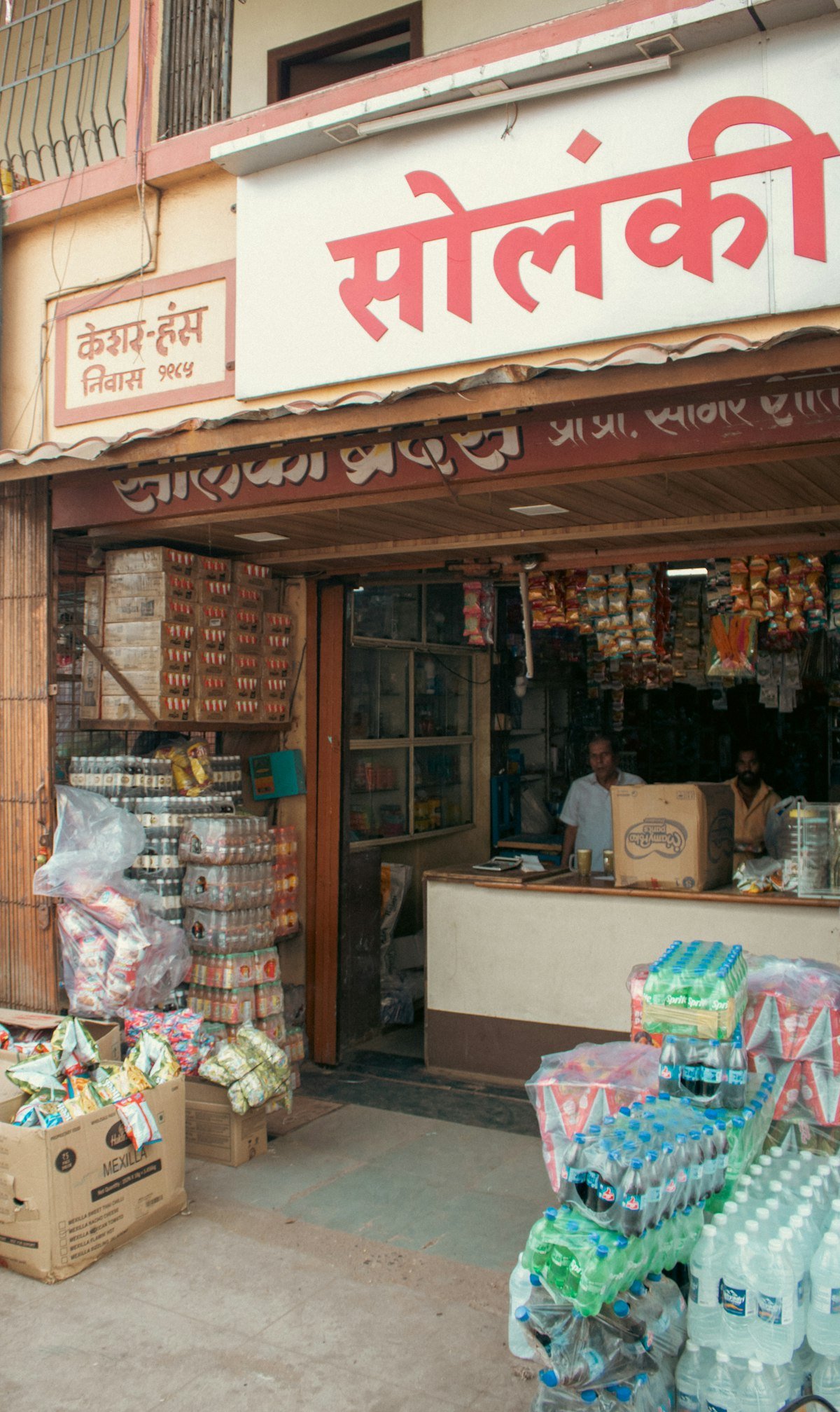 A small Indian general store, the owner standing behind the counter with goods on shelves