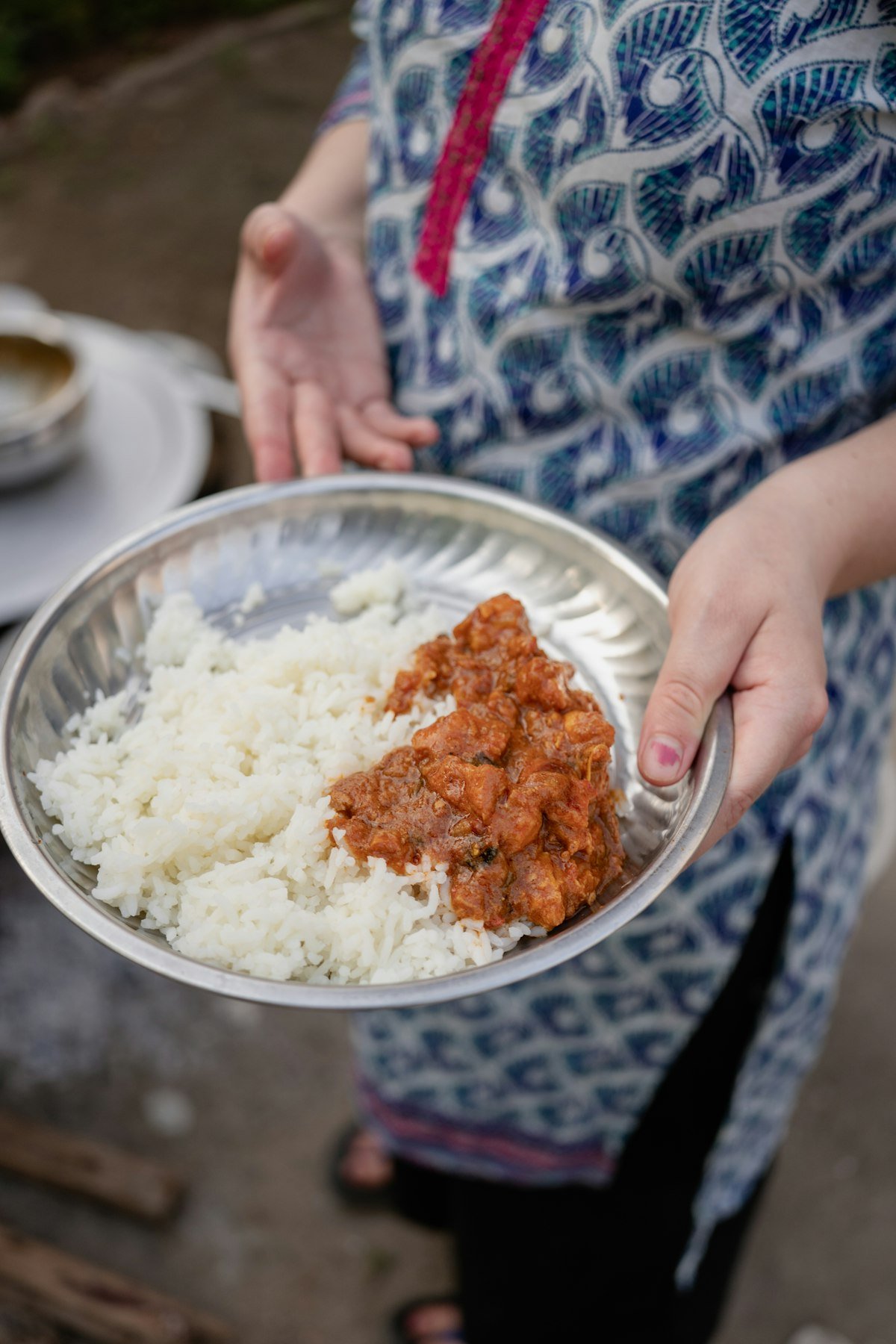 A hand holding a steel plate of rice and curry