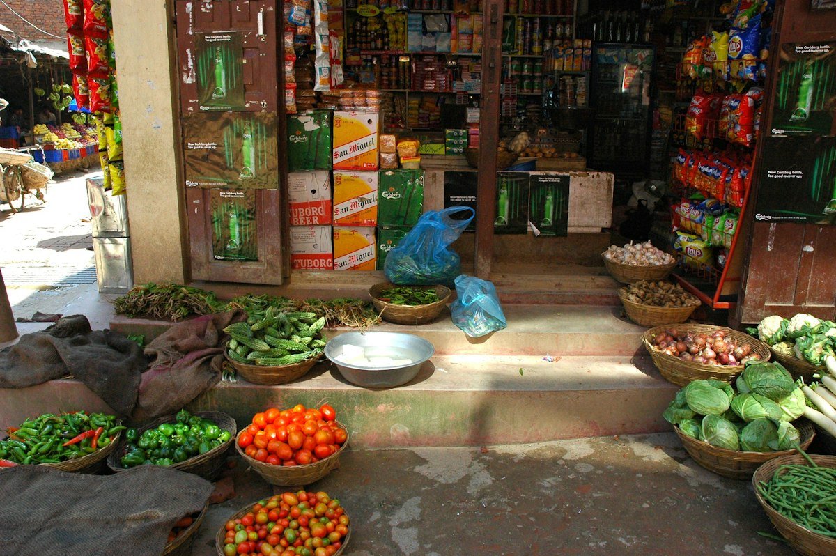 A small shop front with fresh vegetables in baskets and packaged goods on shelves