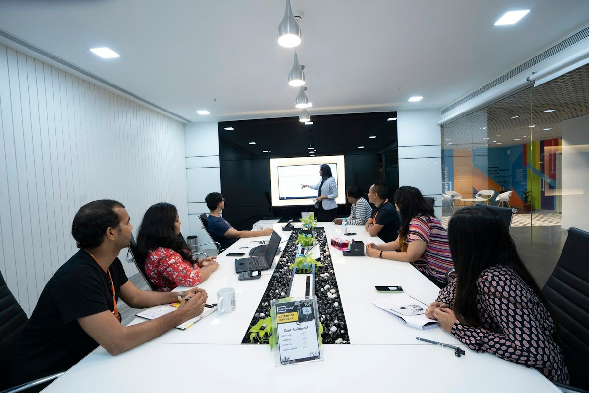 A team training session in a meeting room, with people seated at a long table watching a presenter and a screen