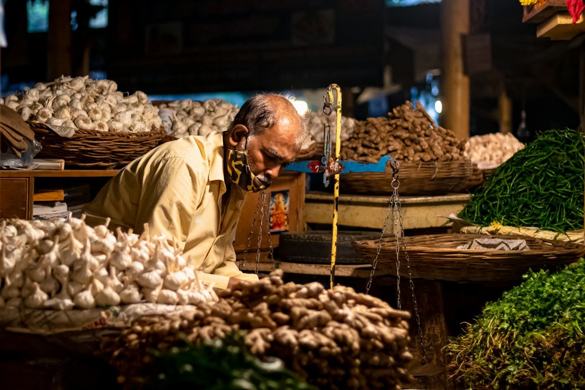A vegetable seller at a market stall with baskets of garlic and produce