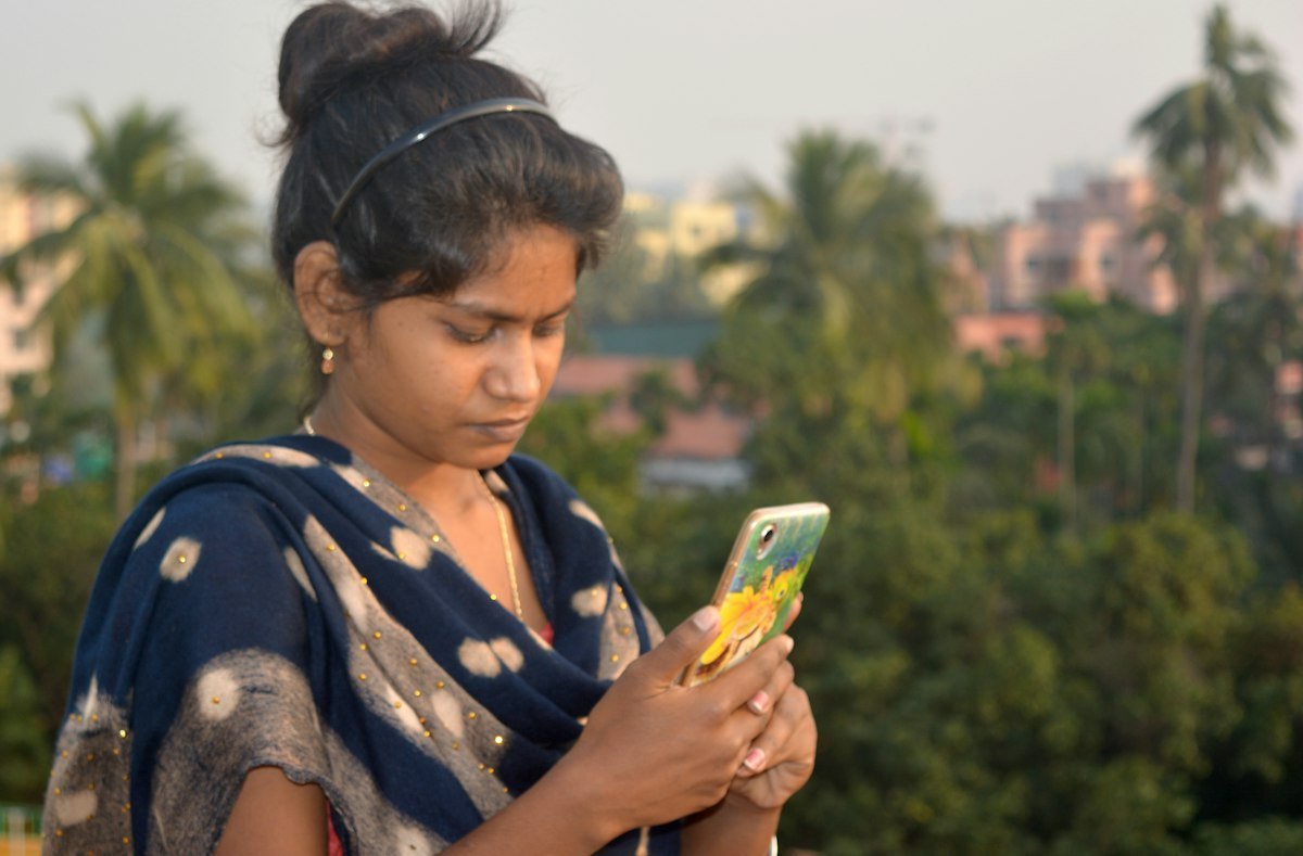 A young Indian woman outdoors looking closely at her mobile phone