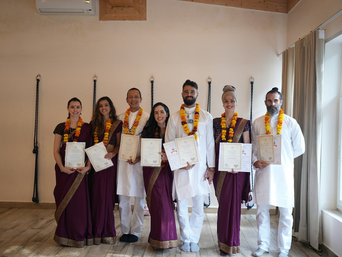 A group of yoga participants in Indian clothes holding certificates and wearing garlands indoors